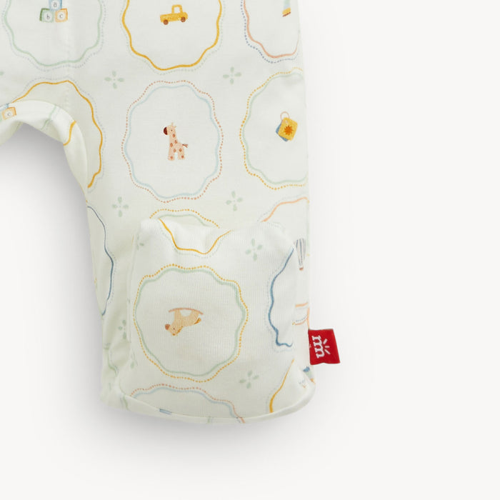 A close-up of a baby bootie featuring a white fabric body with a colorful pattern of yellow, blue, and orange decorative frames containing small animal and object illustrations. A red fabric brand tag is visible on the side.