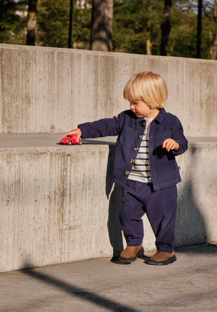 Child in a navy outfit playing with a red toy car on a concrete surface.