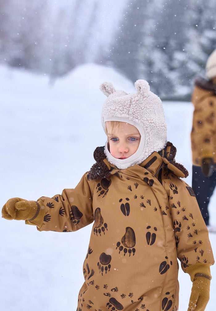 Child in a brown snowsuit with bear paw prints standing in the snow.