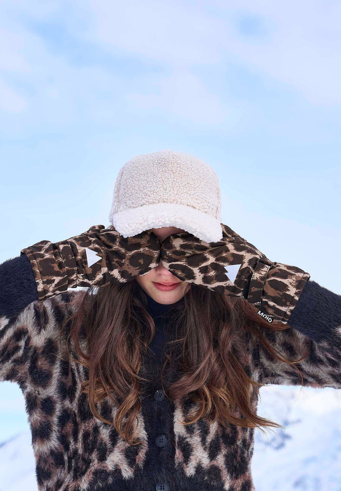 Person wearing a fleece cap and leopard coat against a blue sky