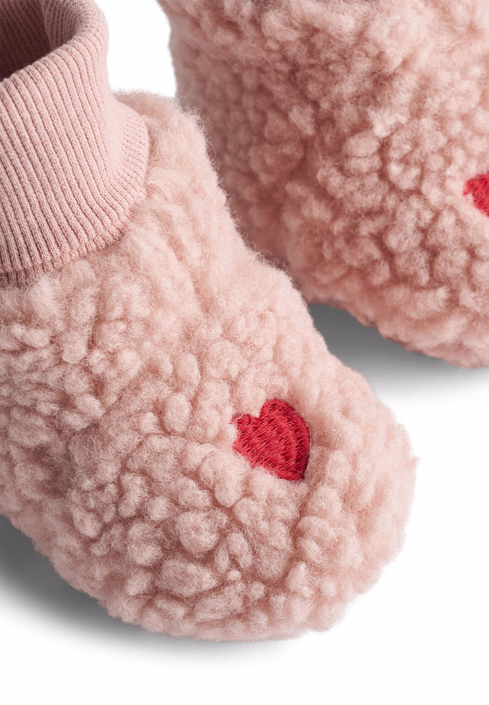 Pink fuzzy baby shoes with red hearts on a white background
